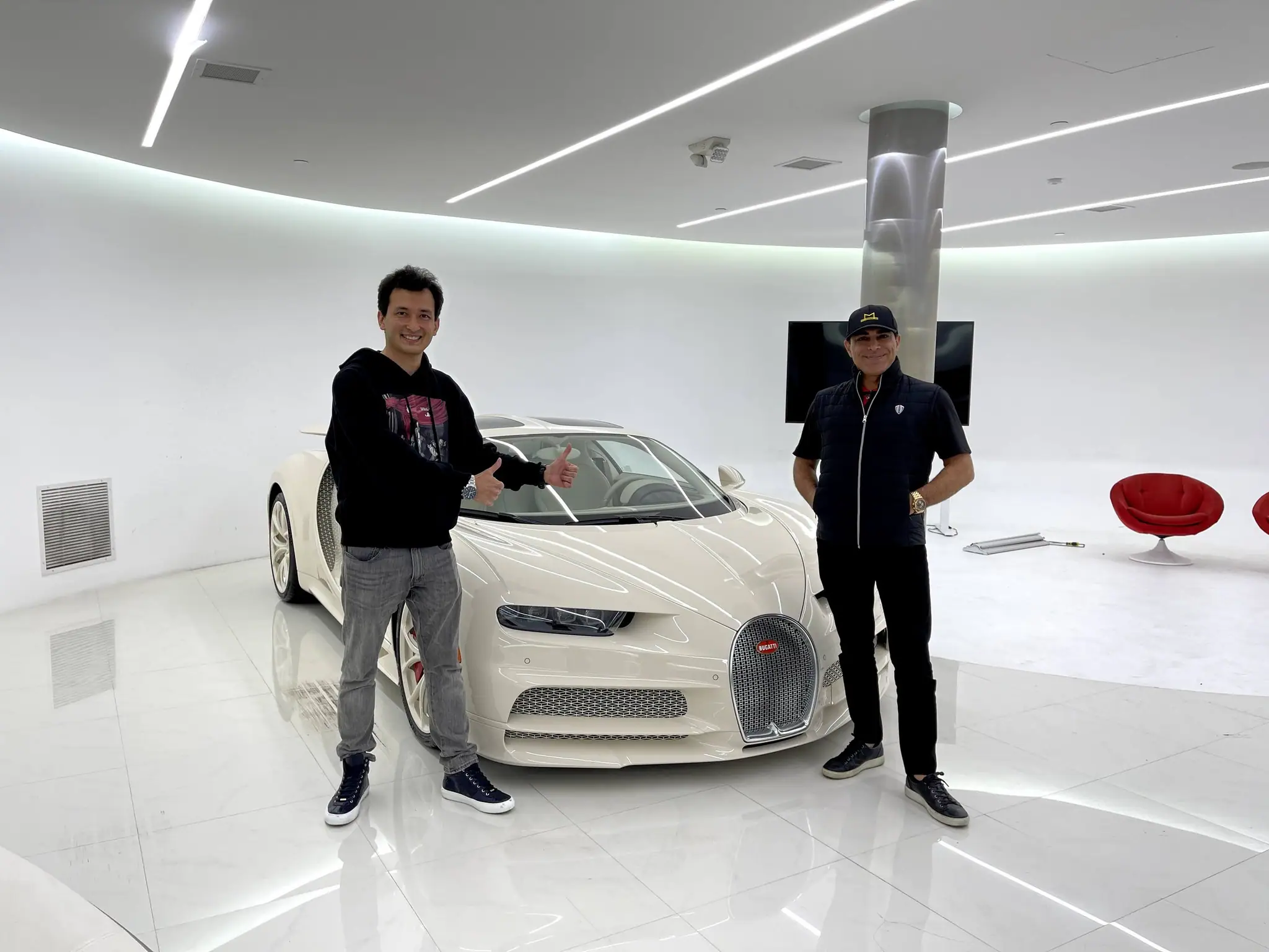 Alan with a host beside a white Bugatti in a bright showroom