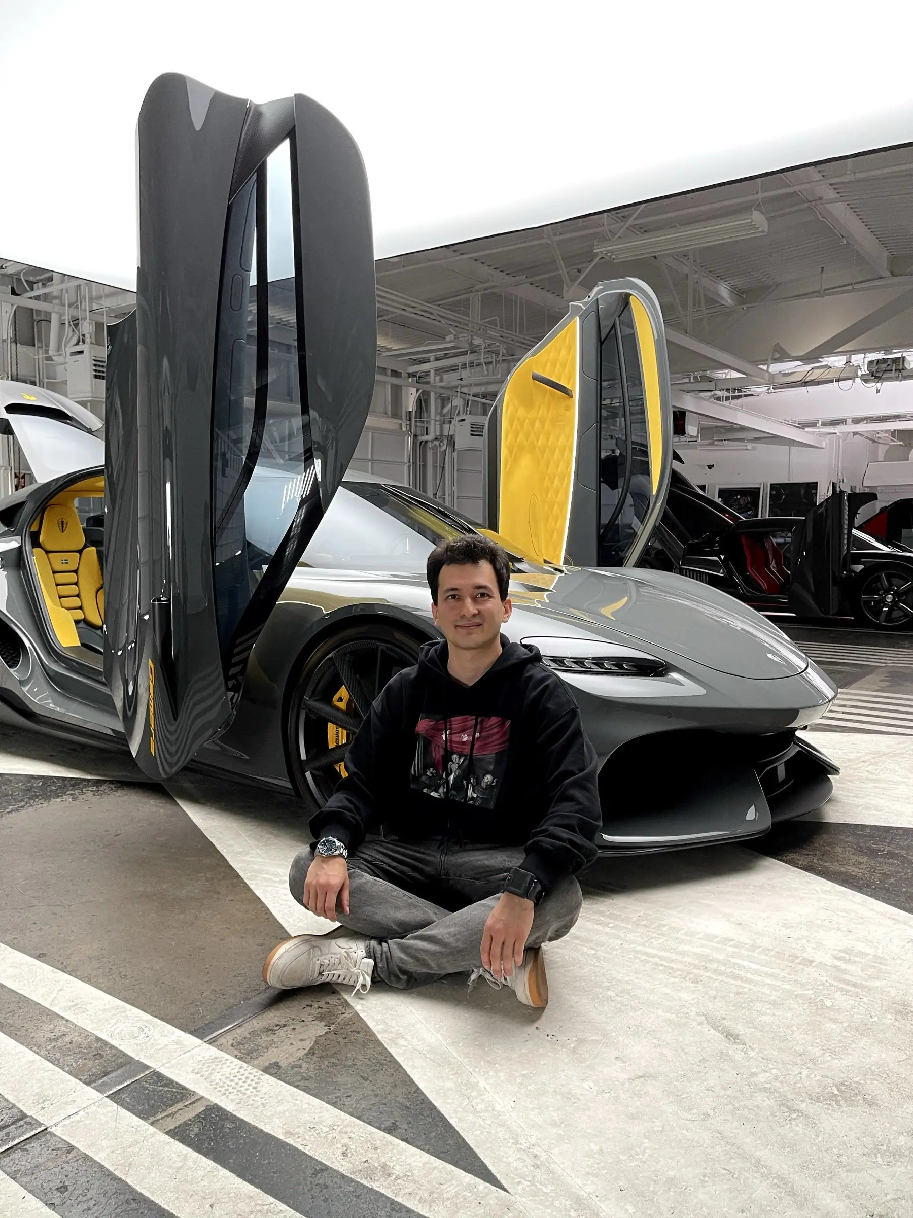Alan sitting in front of a grey hypercar with dihedral doors raised