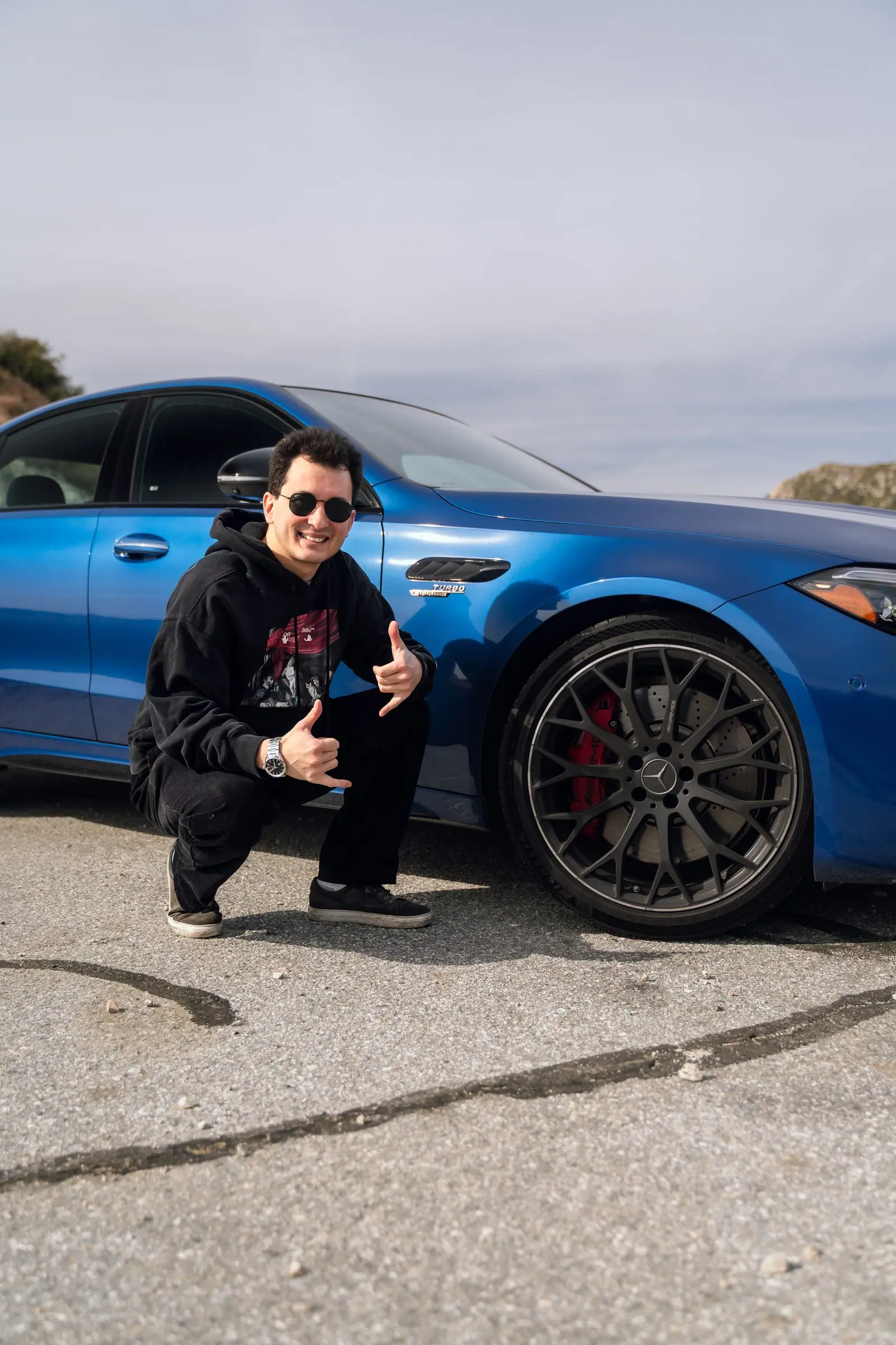 Alan crouching beside the front wheel of a blue Mercedes-AMG C 63
