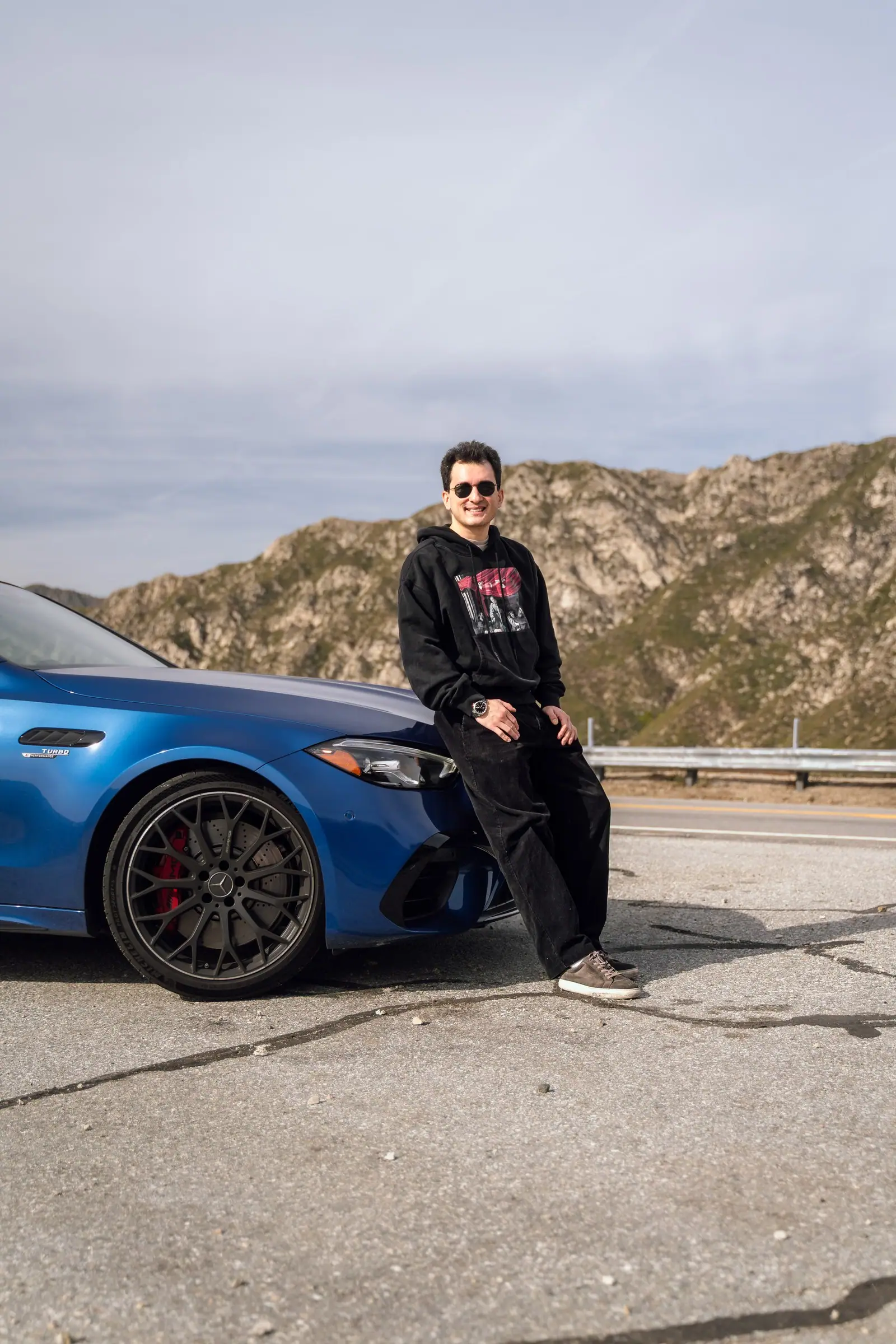 Alan leaning on a blue Mercedes-AMG C 63 with mountains behind