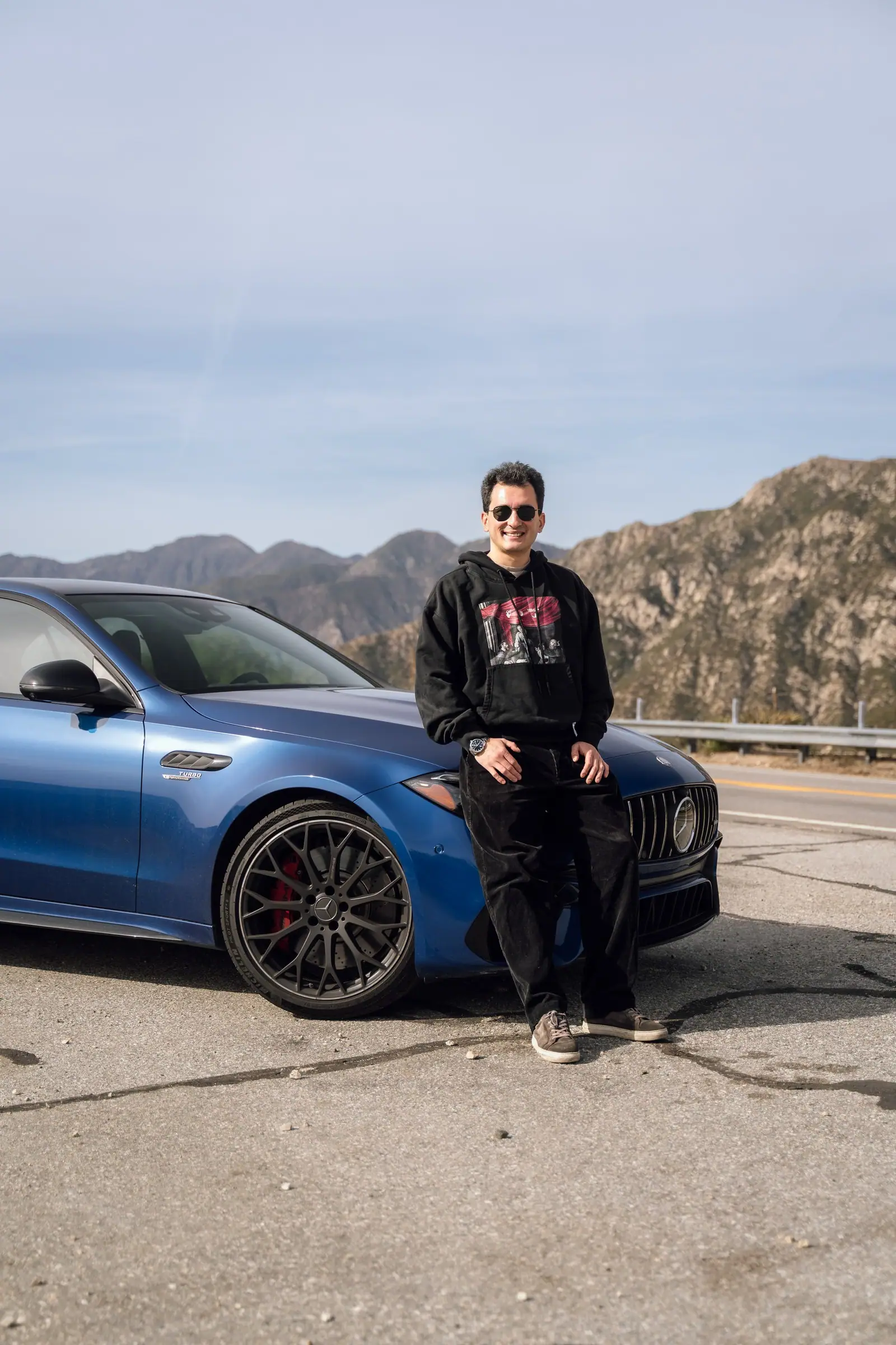 Portrait of Alan Enileev crouching beside a blue Mercedes-AMG C 63