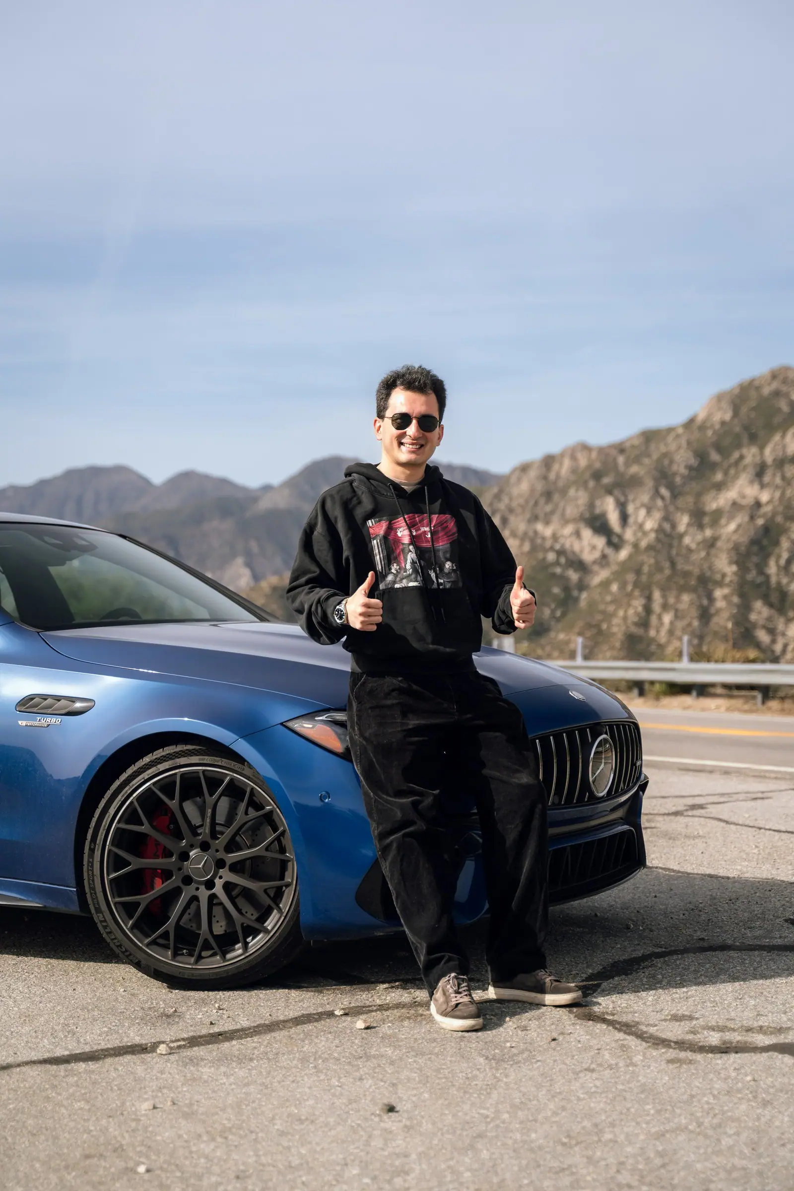 Alan standing by a blue Mercedes-AMG C 63 against a mountain ridge