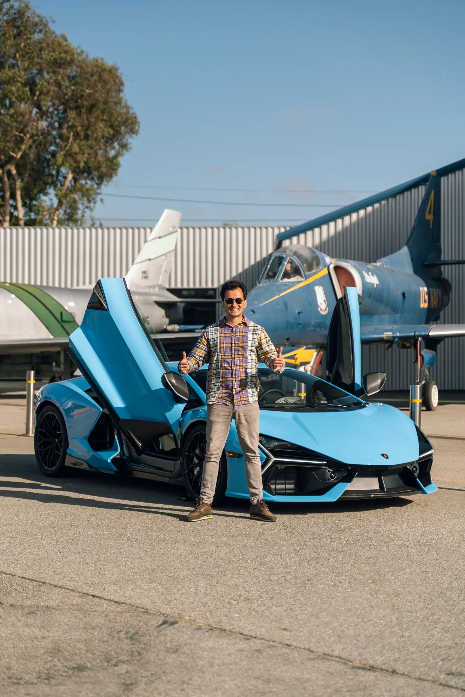 Alan beside a blue Lamborghini Revuelto in front of vintage jet aircraft